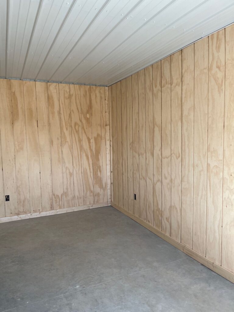 Finished post-frame horse barn interior with wood paneling, white metal ceiling, and concrete floor near the Flint Hills, Kansas