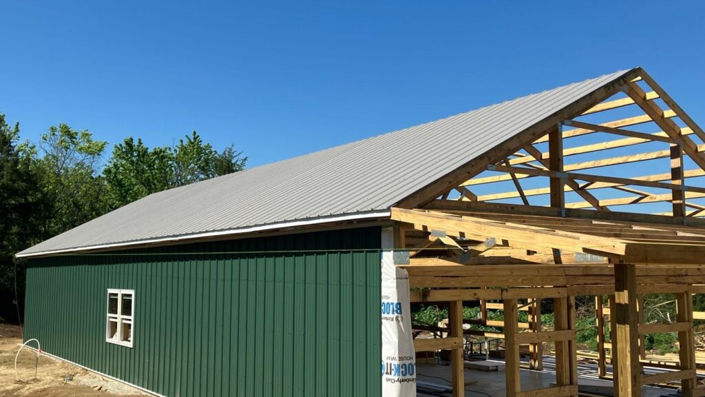 Green metal building under construction with exposed wooden frame.