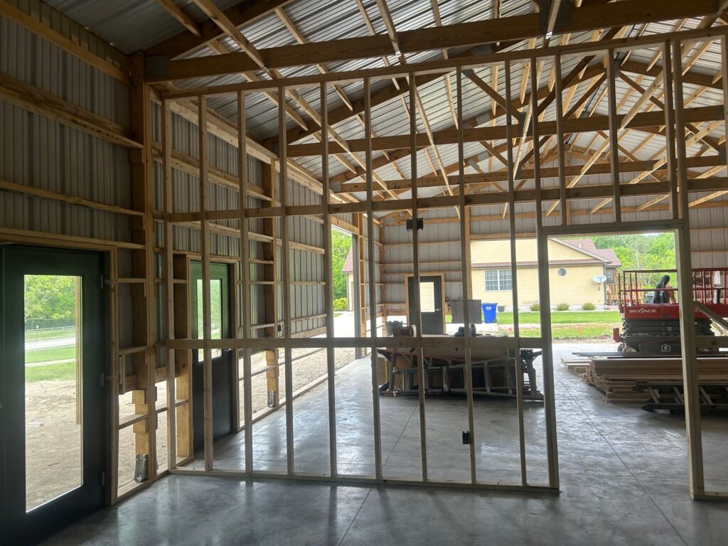 Interior of a partially framed building under construction, with exposed wooden studs and roof trusses.